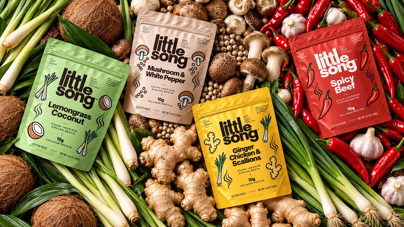 All four Little Song sipping broth pouches on a bed of fresh ginger, scallions, lemongrass, coconuts, mushrooms, white peppercorns, red chilies, and garlic